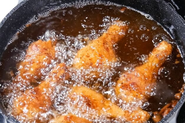 Chicken drumsticks frying in hot oil during the second fry, with bubbles surrounding their crispy, golden-brown crust.