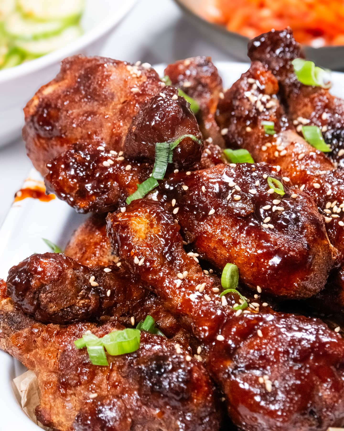 Close-up of Korean fried chicken drumsticks glazed with sweet-and-spicy Yangnyeom sauce, topped with sesame seeds and green onions.