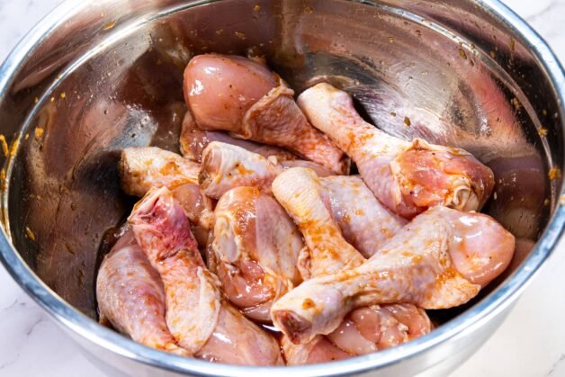 Raw chicken drumsticks marinating in a soy sauce-based marinade inside a stainless steel mixing bowl.