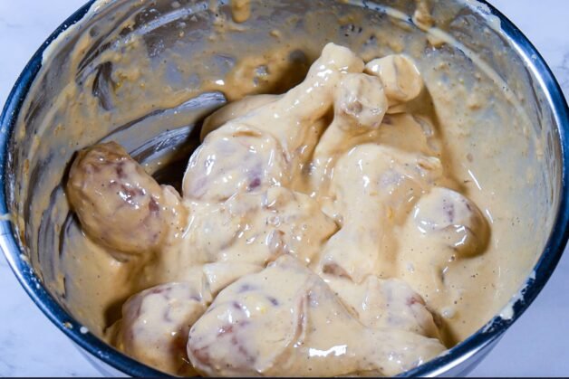 Chicken drumsticks coated in a thick batter mixture in a stainless steel mixing bowl, ready for frying.