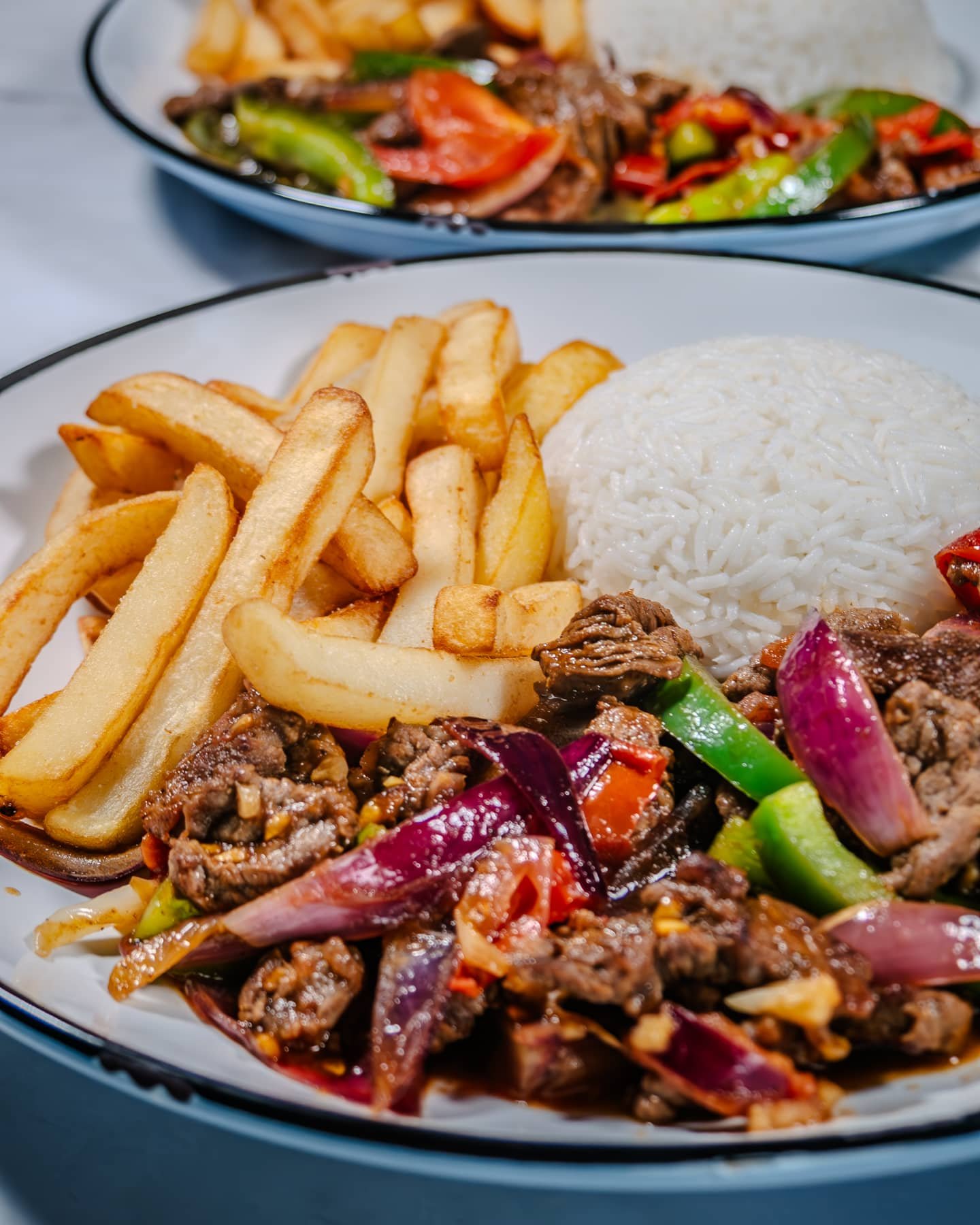 Two servings of Lomo Saltado with stir-fried vegetables, French fries, and rice.