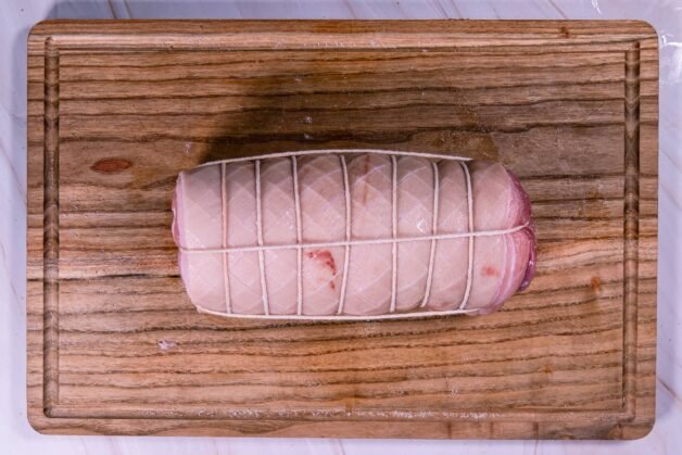 Pork belly roll tightly tied with kitchen twine on a wooden cutting board.
