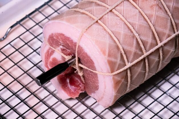 Pork belly roll with a meat thermometer inserted before roasting.