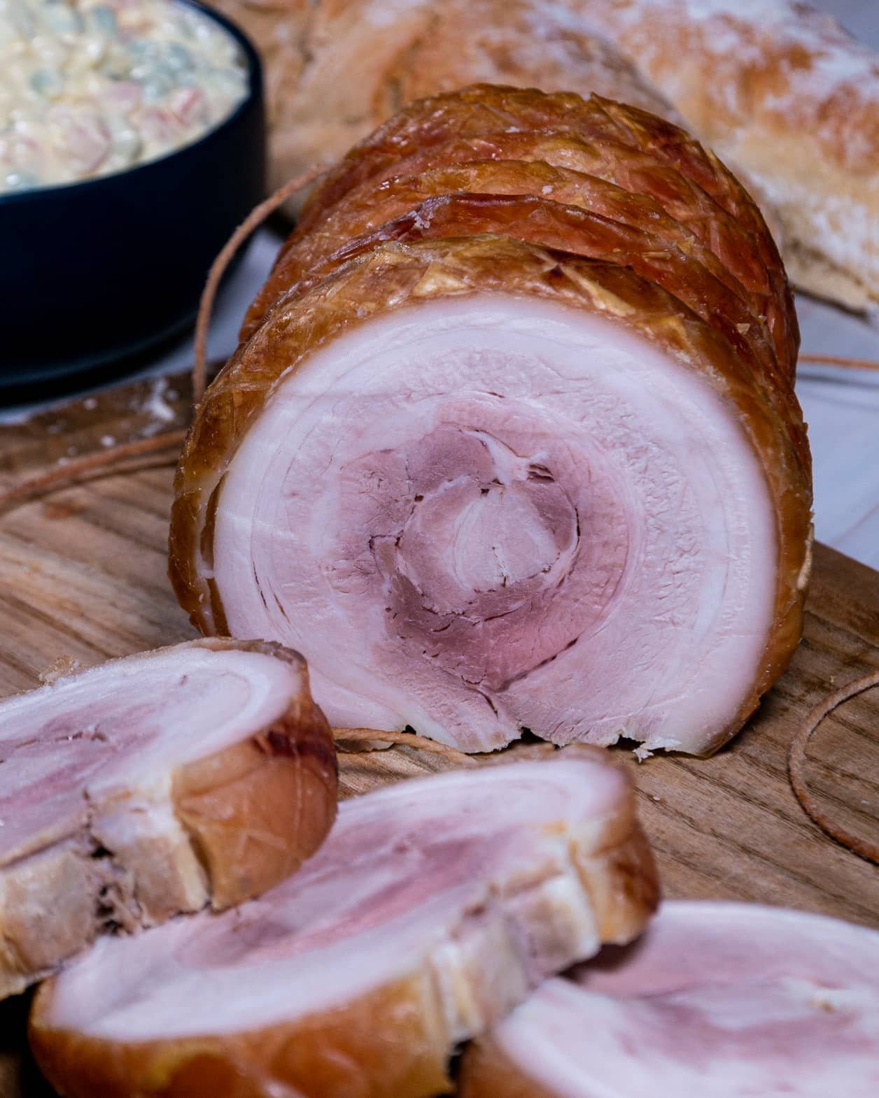 Pork belly roll with slices, served alongside Russian salad and crusty bread.