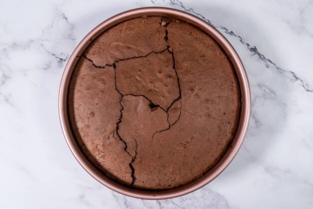 A freshly baked chocolate cake in a round baking pan with a slightly cracked surface, ready to be used as the base for dessert cups