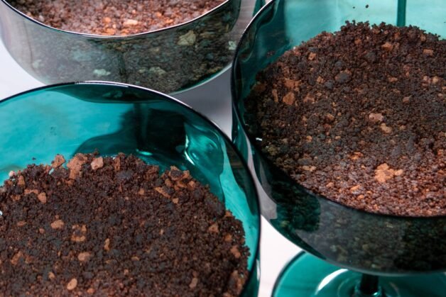 Three green dessert cups filled with a layer of crumbled chocolate cake, evenly pressed into the base.