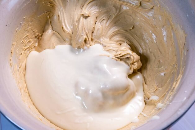 A creamy pistachio mixture combined with melted white chocolate in a mixing bowl, ready to be blended.