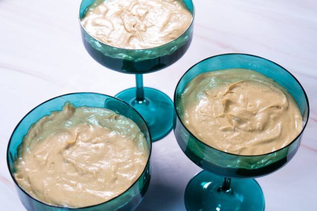 Three dessert cups filled with a smooth pistachio and white chocolate cream layer, evenly distributed.