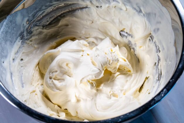 Soft peaks of freshly whipped cream in a metal mixing bowl.