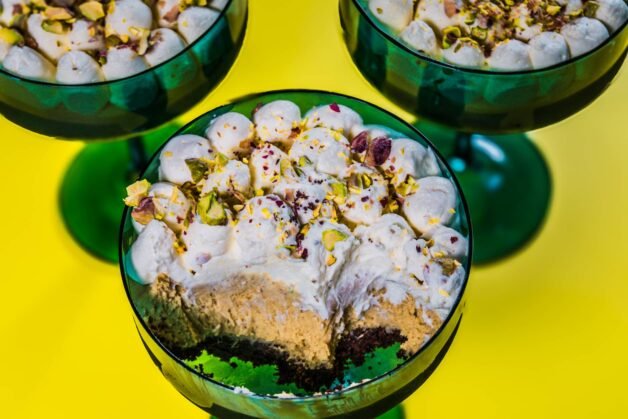 A dessert cup with a spoonful taken out, revealing the rich chocolate, pistachio cream, and whipped cream layers.