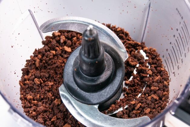 Crumbled chocolate cake base in a food processor, showing finely crushed chocolate crumbs ready for layering in dessert cups.