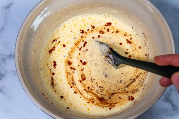 Egg and sugar mixture combined with melted chocolate and butter, stirred with a spatula in a mixing bowl.