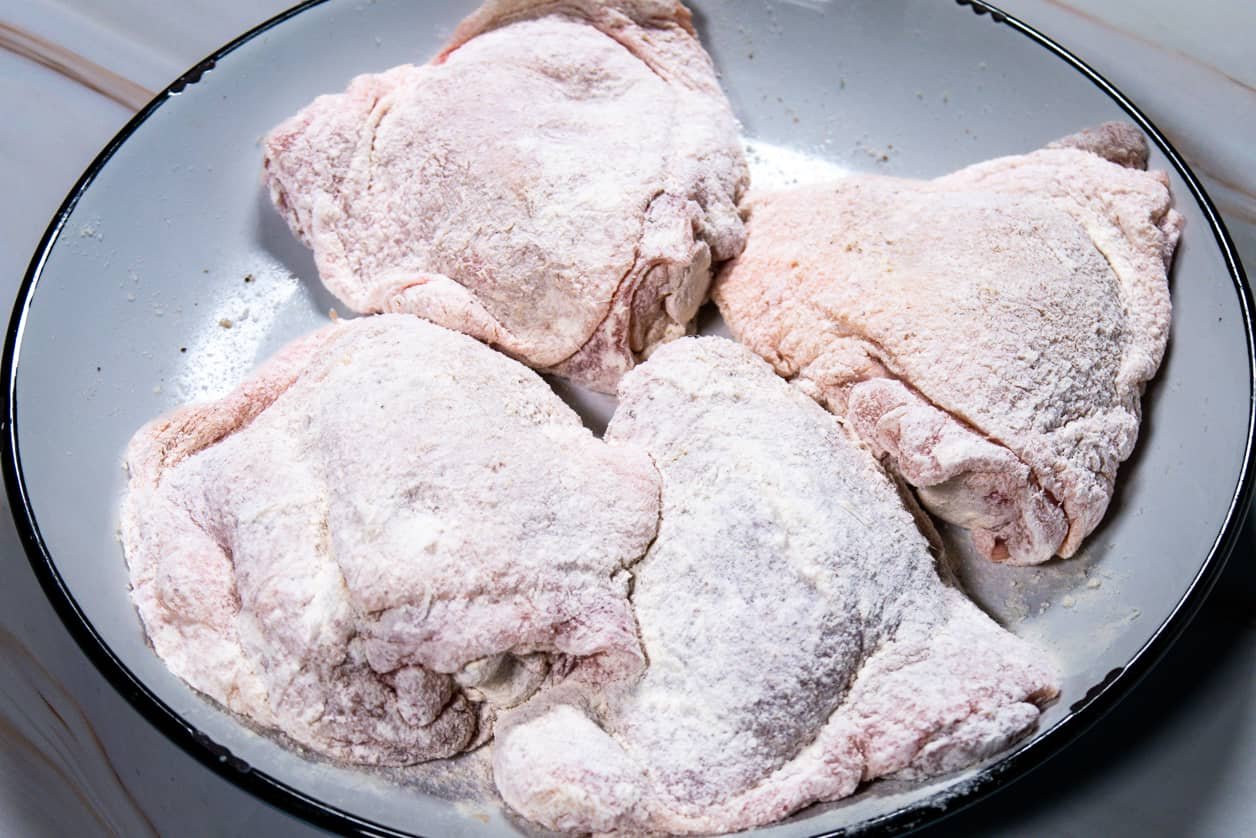Chicken thighs fully coated in flour, ready for searing.