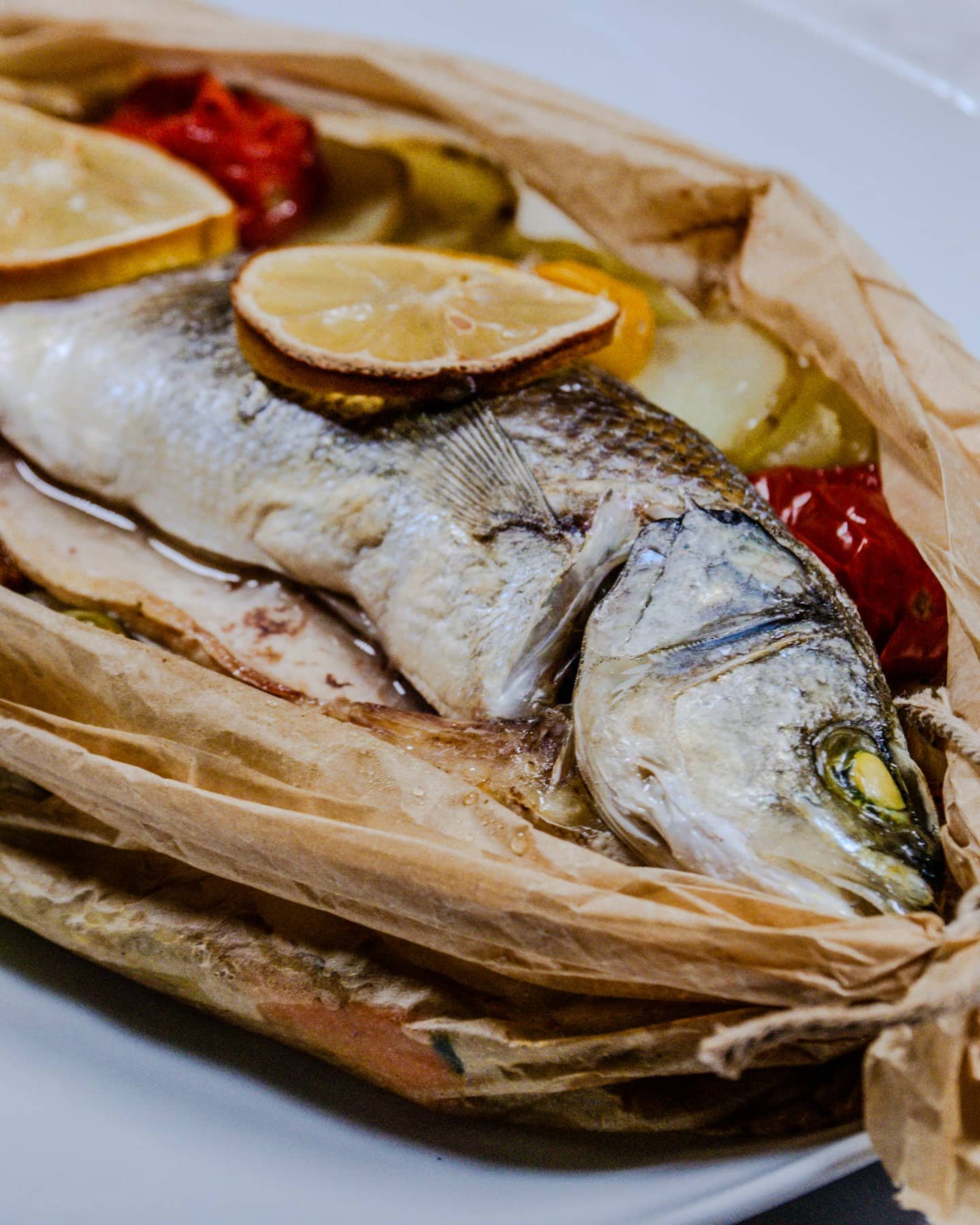 Cooked Sea Bass en Papillote with lemon slices and vegetables peeking through parchment paper.