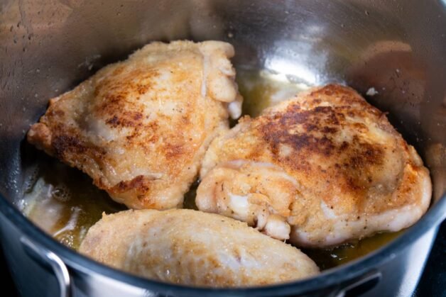 Golden-brown chicken thighs searing in a pot with hot oil.