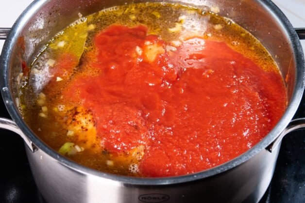 Chicken simmering in broth with tomato sauce added on top in a pot.