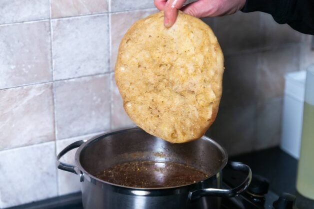 Traditional Balkan flatbread being dipped in a flavorful beef and vegetable broth for cevapi preparation.