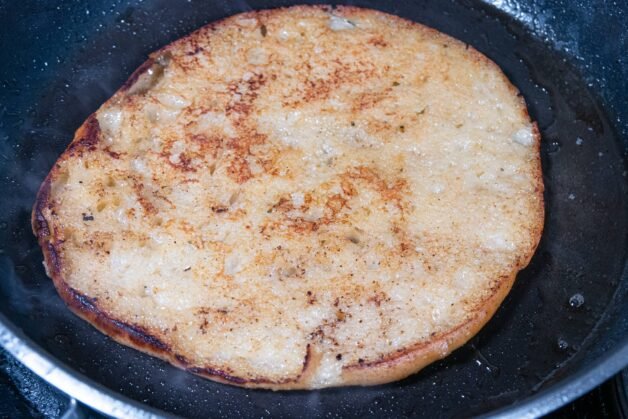Traditional Balkan flatbread toasting in a skillet after being dipped in broth.