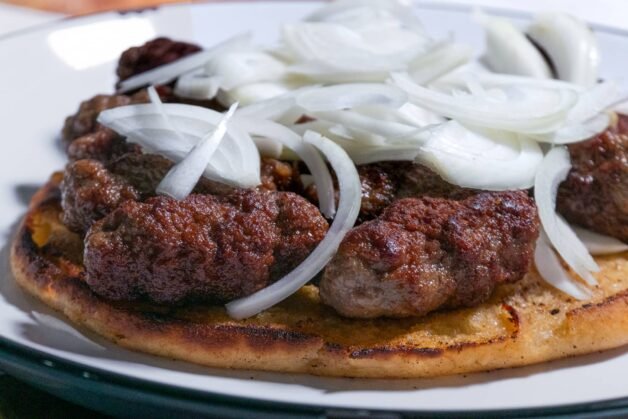 Juicy cevapi served on golden flatbread, topped with fresh sliced onions.