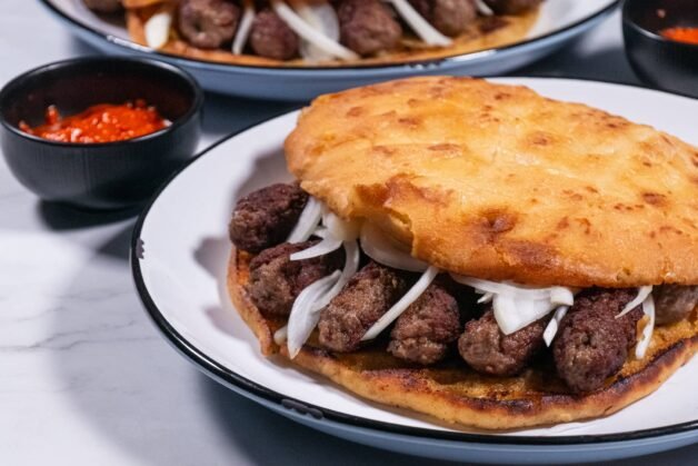 A traditional Balkan cevapi sandwich served with ajvar, onions, and golden flatbread.