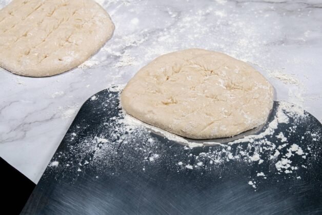 Shaped flatbread dough on a floured pizza peel, ready for baking.