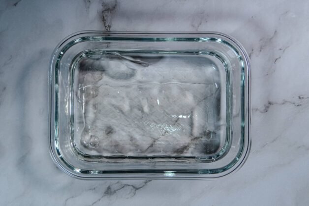 Sheet gelatin soaking in a glass container filled with cold water.
