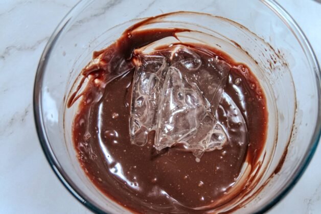 Softened sheet gelatin added to melted chocolate mixture in a glass bowl.