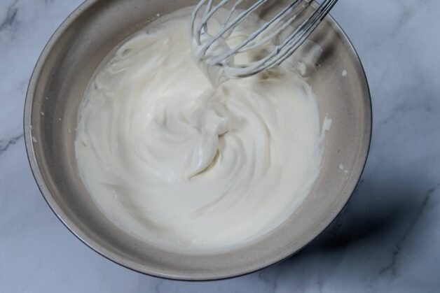 Softly whipped heavy cream in a mixing bowl with a whisk.