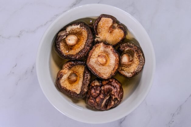 A bowl of rehydrated shiitake mushrooms soaking in water, ready for cooking.