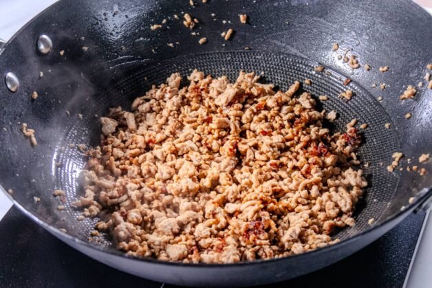 Ground pork browning in a wok, releasing rich flavors and forming a crispy texture.