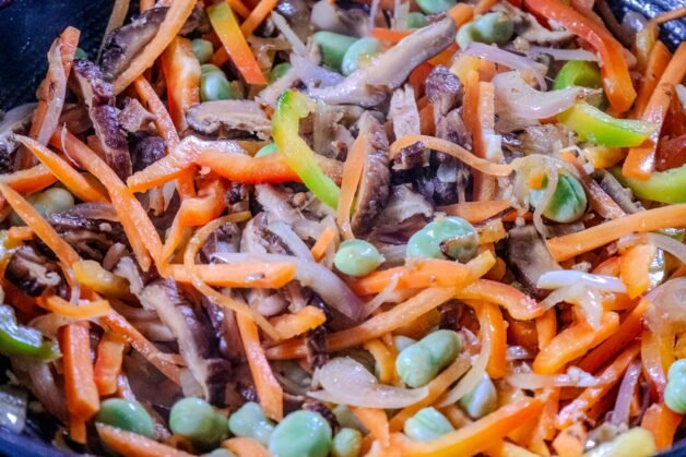 Stir-fried shiitake mushrooms, carrots, bell peppers, and broad beans sizzling together in a wok.
