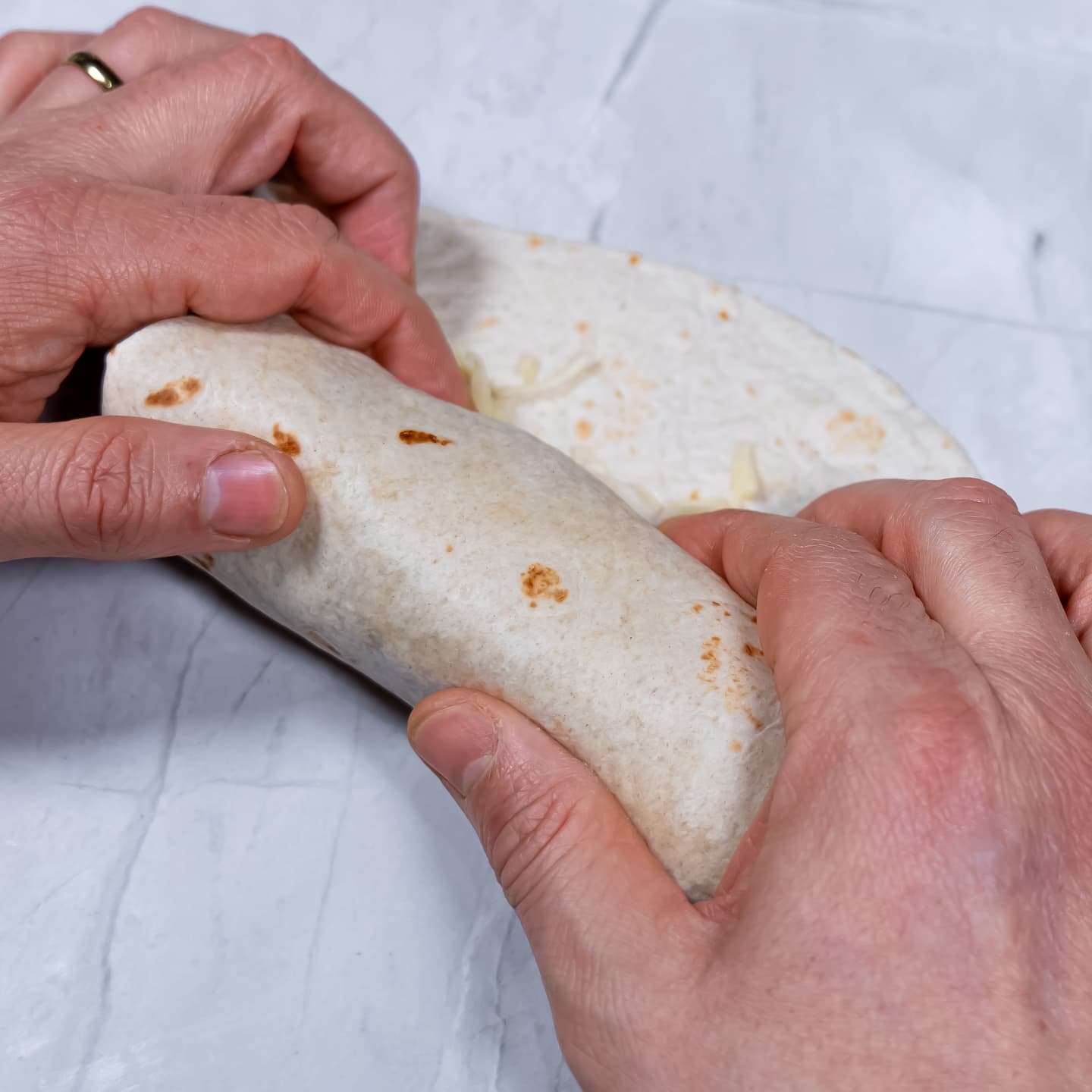 Hands rolling a burrito tightly to seal the fillings inside.