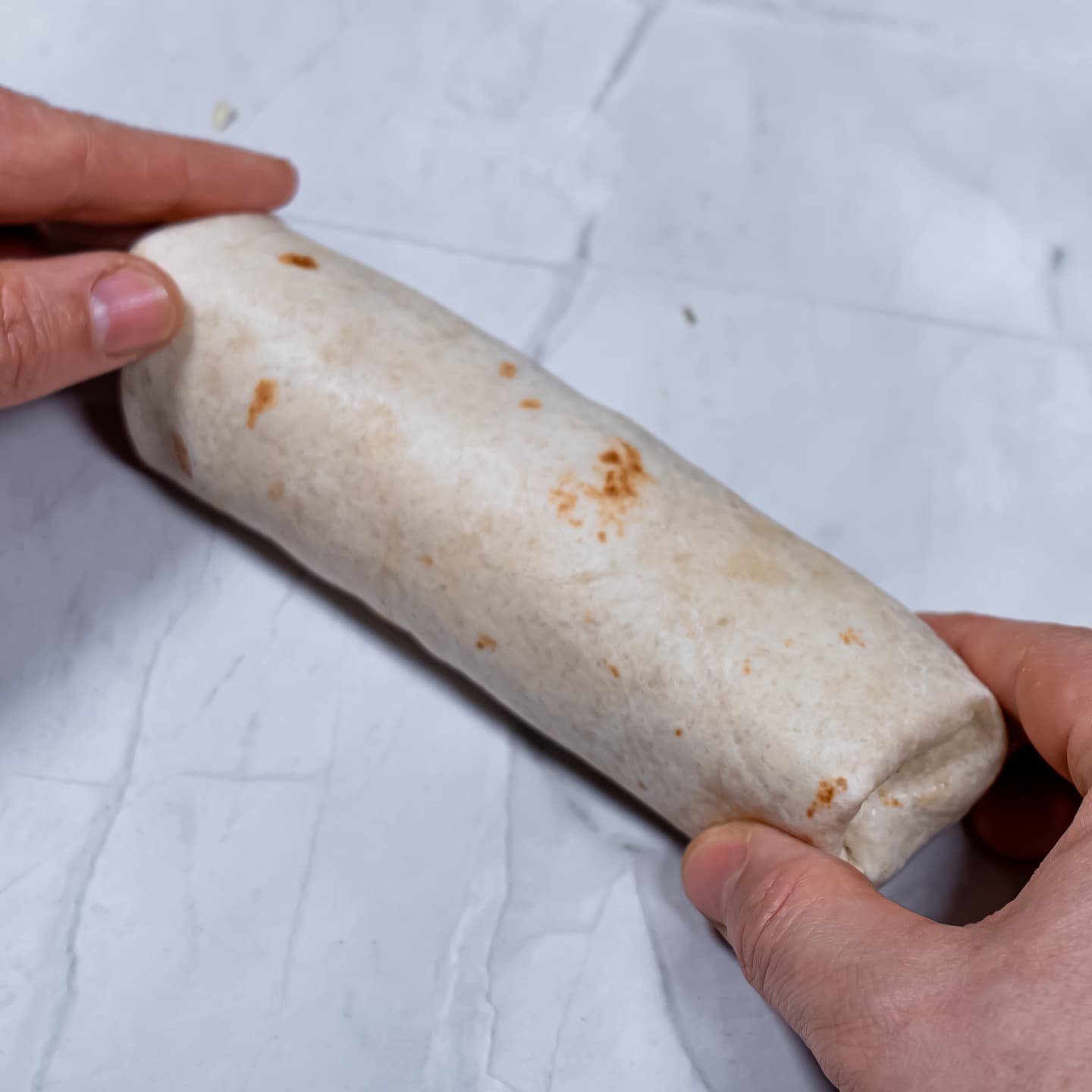 A fully wrapped burrito with both ends sealed, ready for toasting.