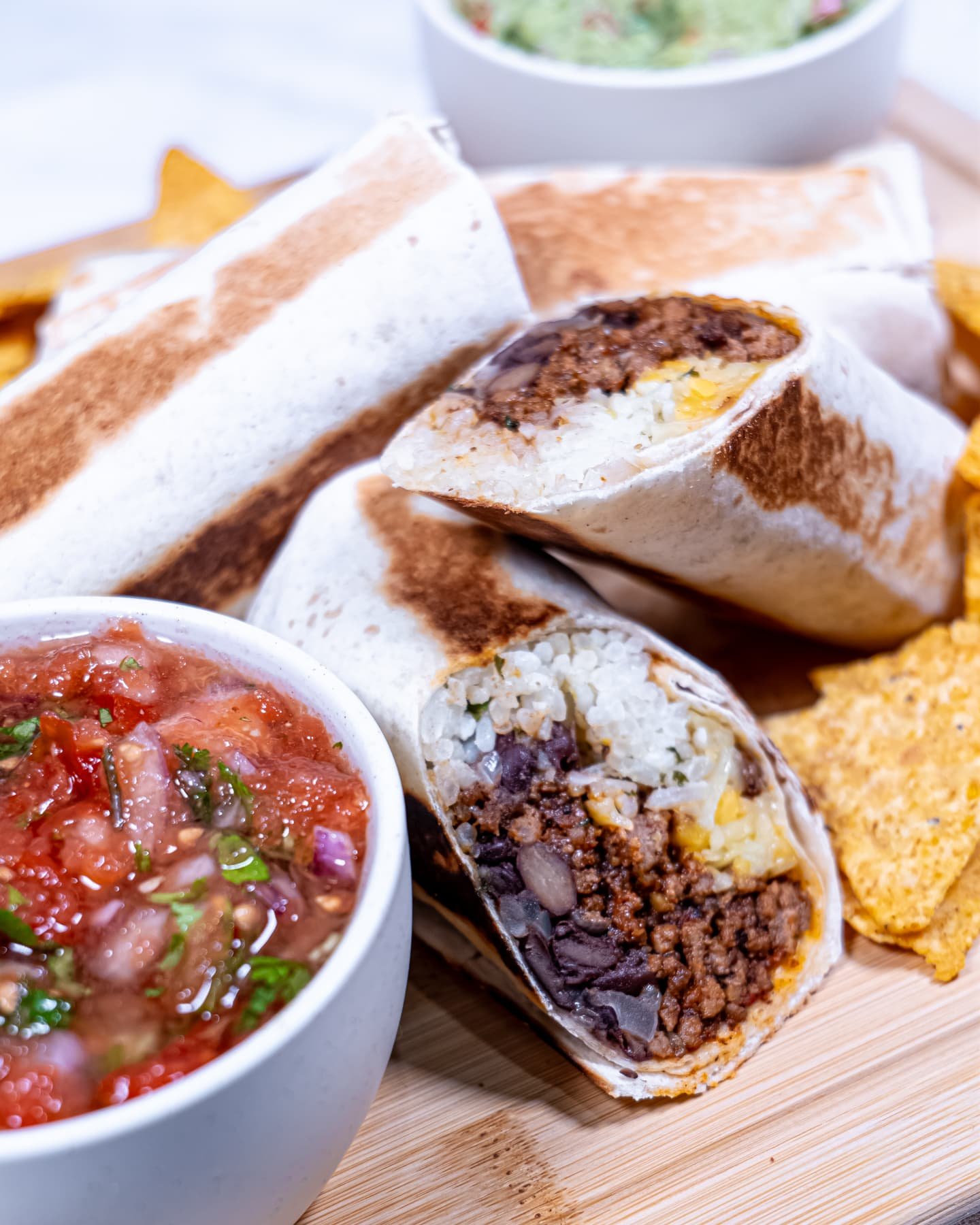A crispy beef burrito cut in half, showing layers of seasoned beef, black beans, cilantro lime rice, and melted cheese, served with salsa.
