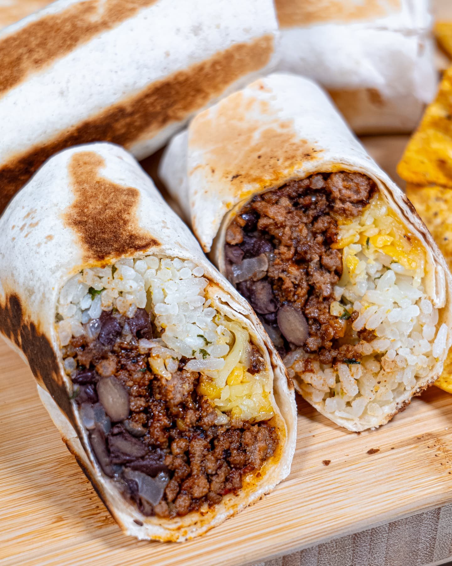 A freshly cut beef burrito showcasing seasoned beef, black beans, cilantro lime rice, and melted cheese inside a toasted tortilla.