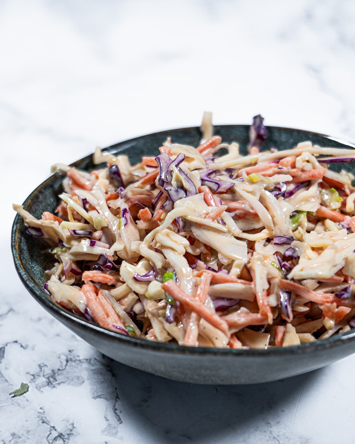 Close-up of creamy coleslaw salad with shredded cabbage, carrots, and a tangy dressing in a dark bowl.
