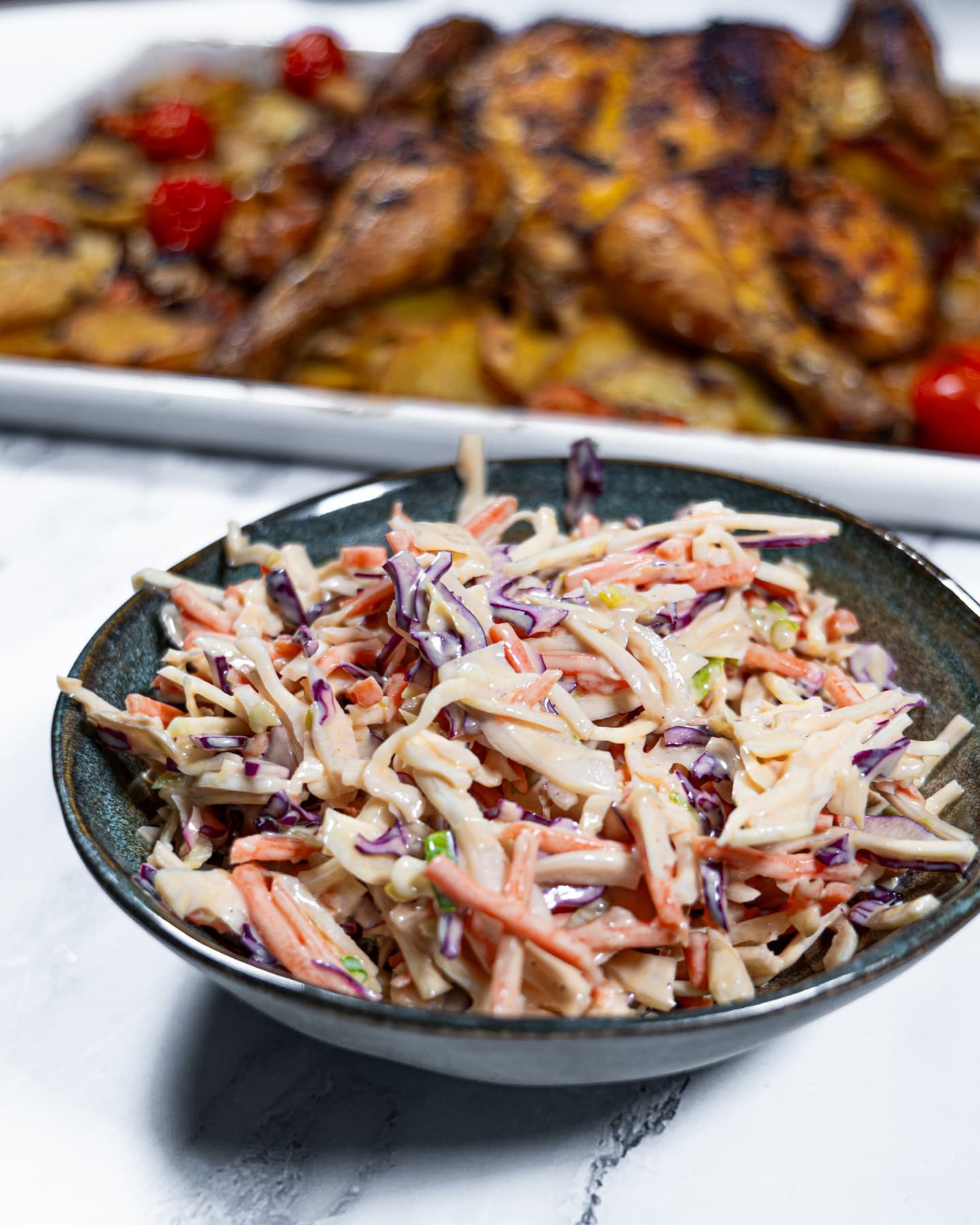 Bowl of creamy coleslaw salad with shredded cabbage and carrots, served alongside roasted chicken and potatoes.