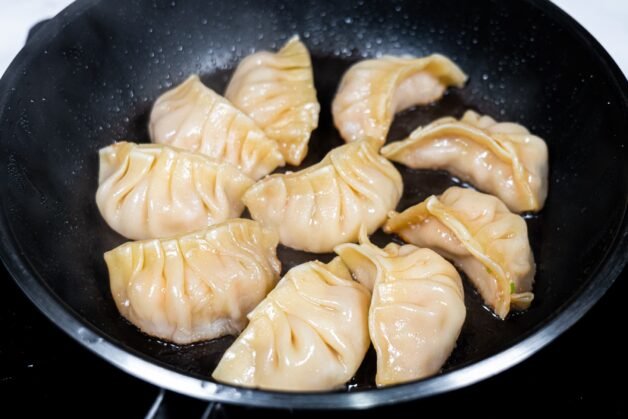Shrimp & pork dumplings sizzling in a pan, cooking to a golden-brown crisp.