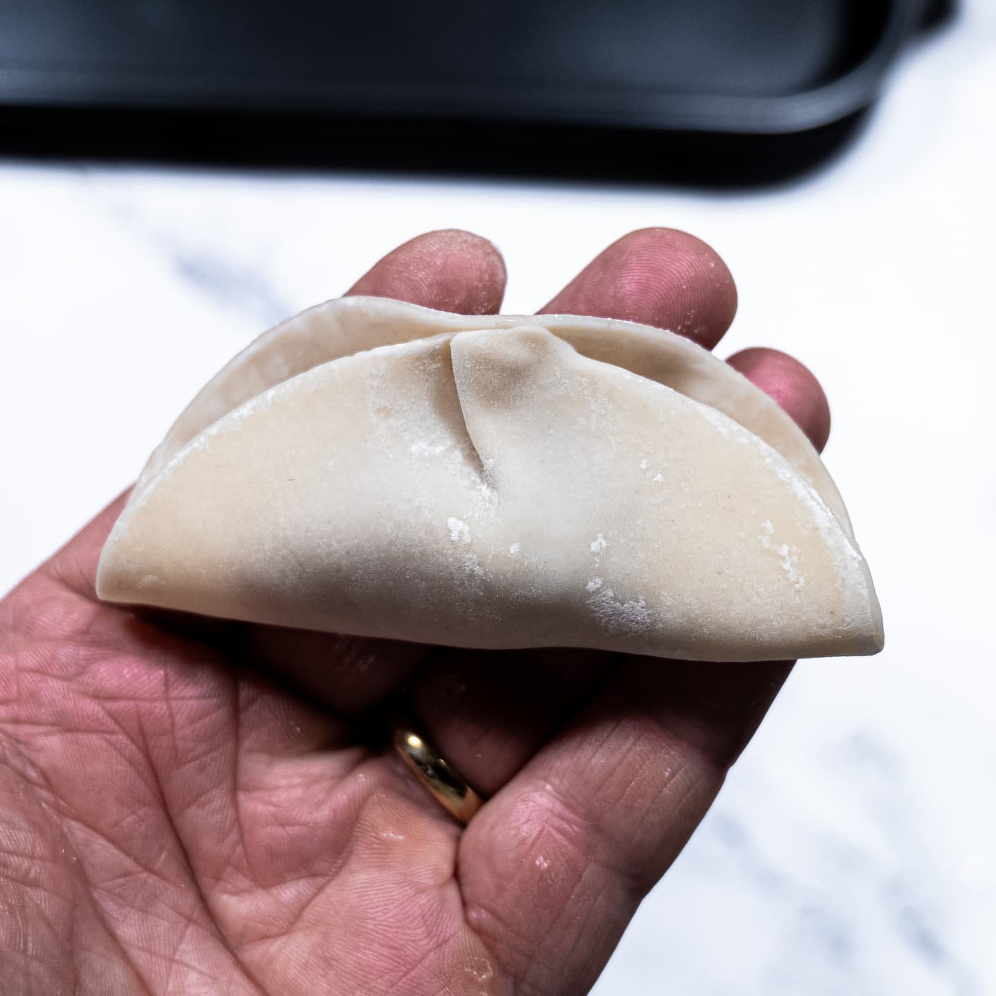 A half-sealed dumpling held in hand, showing how to fold it before pleating.