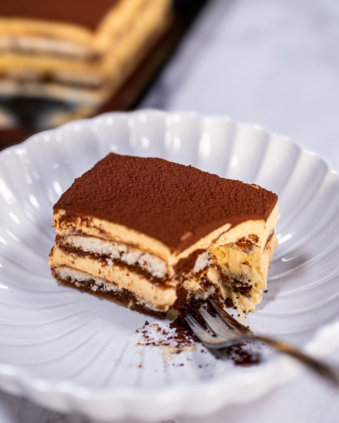 A partially eaten slice of authentic Italian tiramisu on a white plate, showing its creamy mascarpone layers, espresso-soaked ladyfingers, and cocoa dusting.