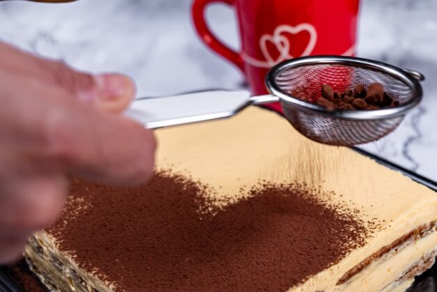 Cocoa powder being dusted over a freshly prepared tiramisu, completing the final layer of this authentic Italian dessert.