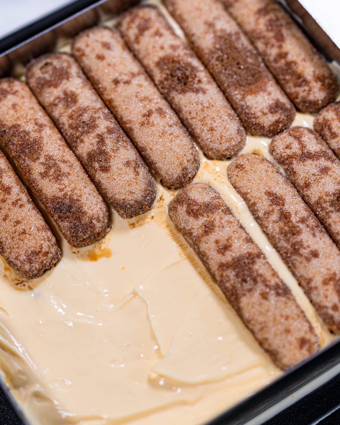 Espresso-soaked ladyfingers layered over mascarpone cream in a baking dish, showing the foundation of an authentic Italian tiramisu.